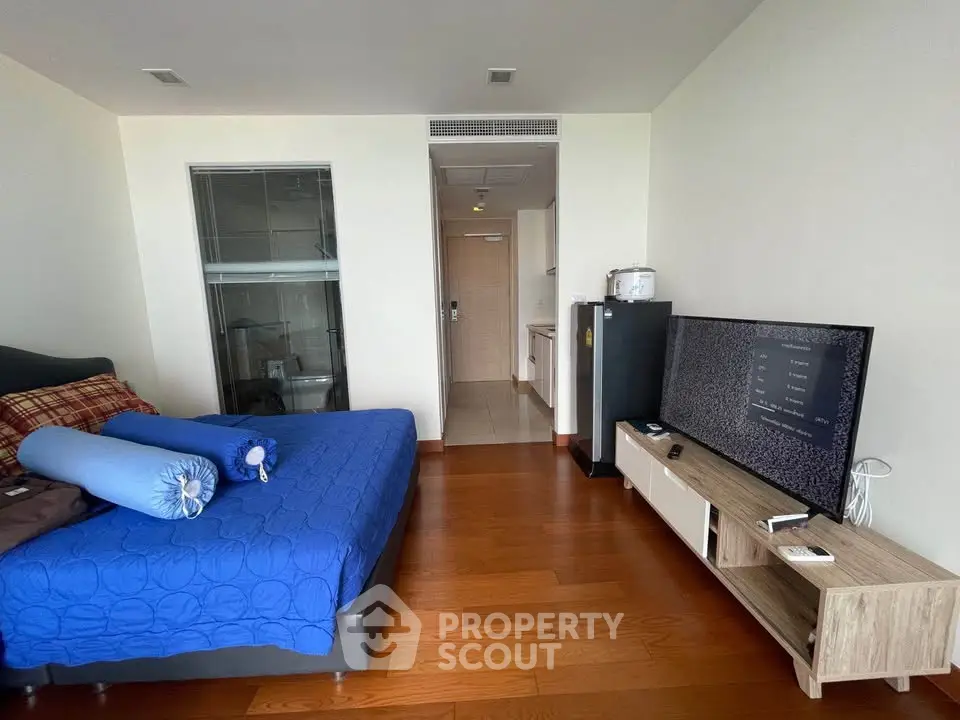 Modern bedroom with wooden flooring, stylish bed, and entertainment unit in a cozy apartment.