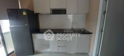 Modern kitchen with sleek cabinetry and black countertop, featuring a refrigerator and stainless steel sink.