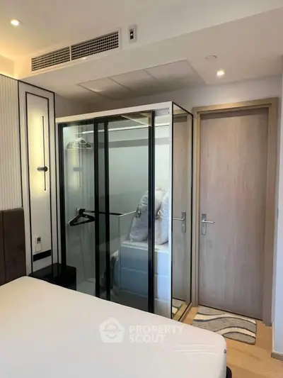 Modern bedroom with glass-enclosed wardrobe and sleek design elements.