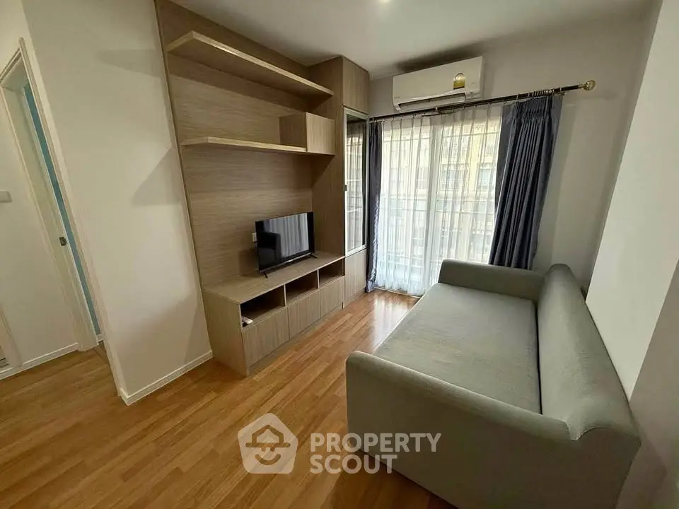 Modern living room with sleek wooden flooring, cozy sofa, and built-in TV unit under natural light.