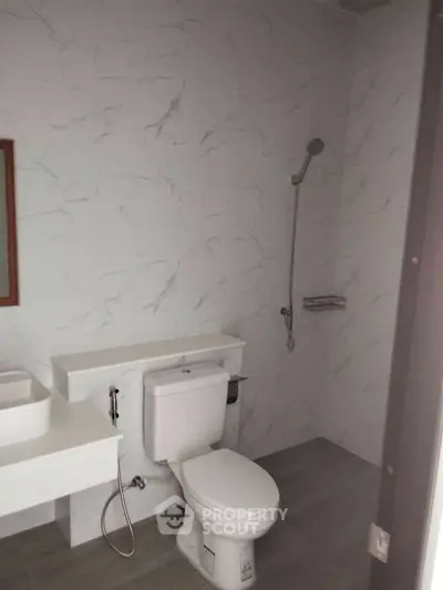 Modern bathroom with sleek design and marble walls, featuring a toilet and shower area.