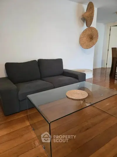 Modern living room with sleek glass coffee table and stylish gray sofa on wooden flooring.