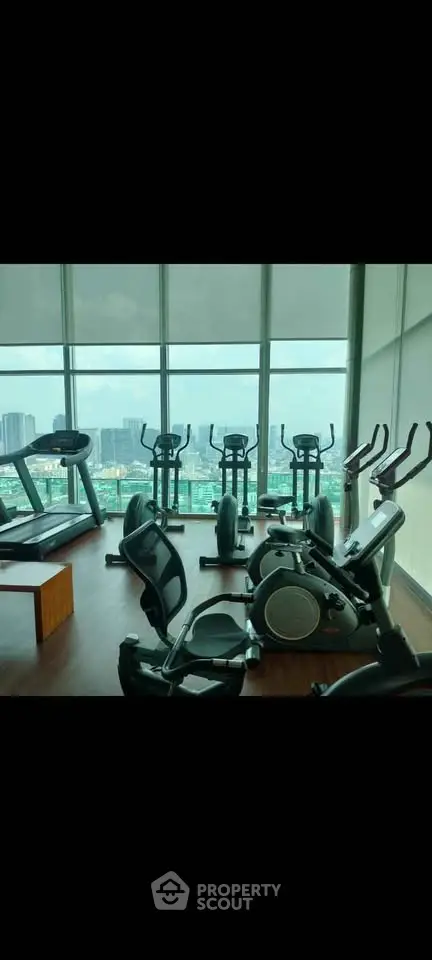 Spacious gym with modern equipment and city view in luxury high-rise building.