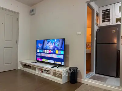 Modern living room with sleek TV setup and adjacent kitchen area featuring stainless steel fridge.