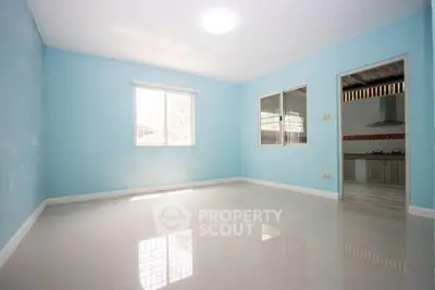 Spacious empty room with blue walls and large windows, adjacent to a modern kitchen.