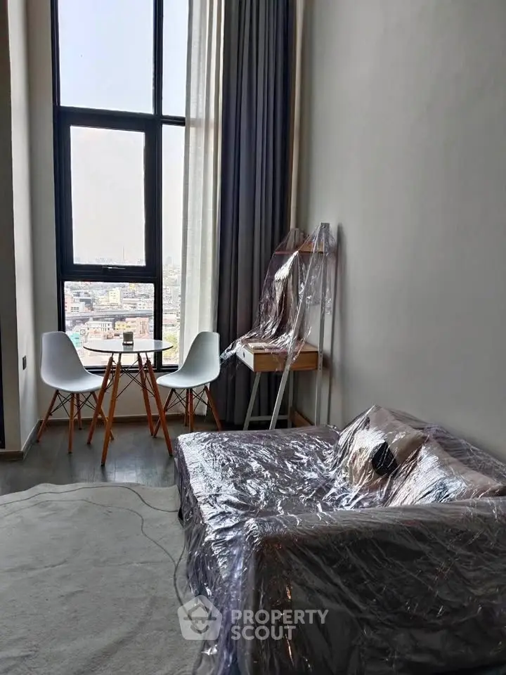 Modern living room with high ceilings and city view, featuring stylish furniture and large windows.