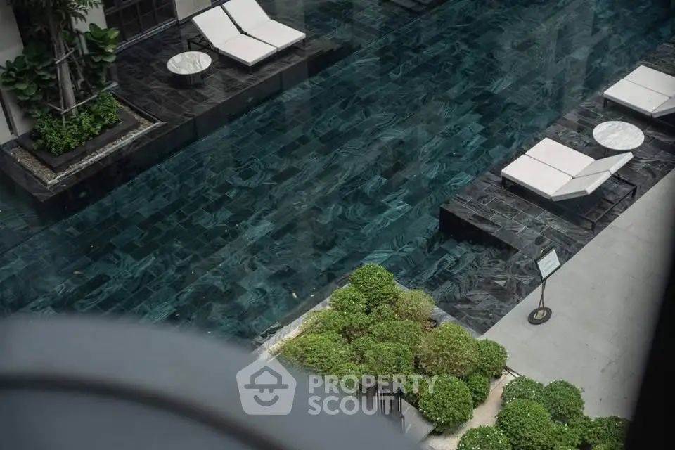 Luxurious outdoor pool area with elegant lounge chairs and lush greenery in a modern real estate setting.