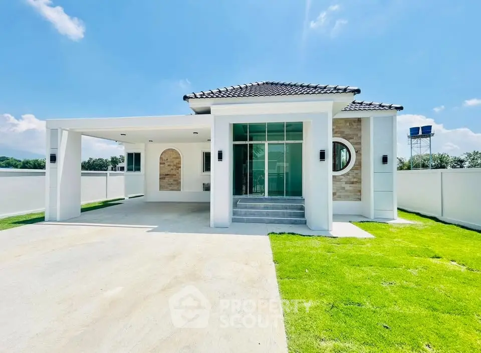 Modern single-story house with spacious driveway and lush green lawn under a clear blue sky.