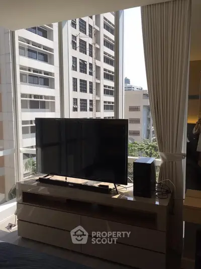 Modern living room with large TV and city view through floor-to-ceiling windows.