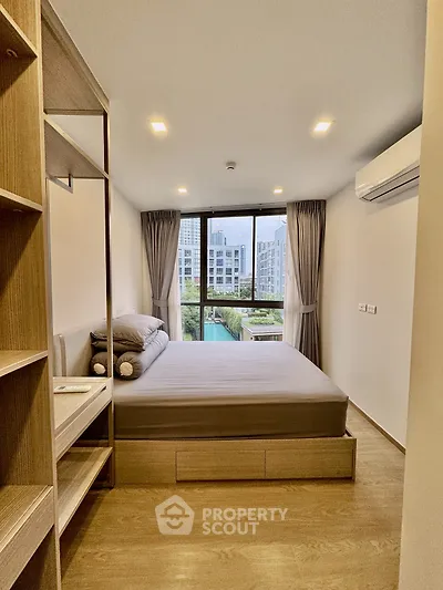 Modern bedroom with large window and city view, featuring sleek wooden furniture and neutral decor.