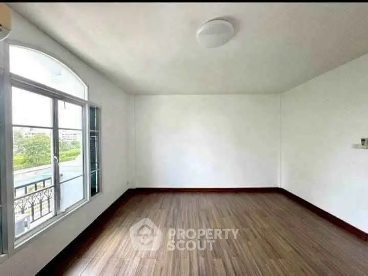 Spacious empty room with large window and wooden flooring, ideal for customization.