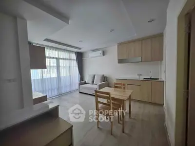 Modern living room with open kitchen, featuring sleek wooden furniture and natural light.