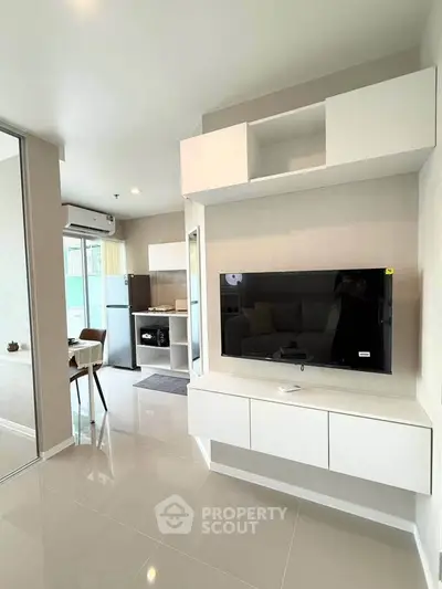 Modern living room with sleek white furniture and wall-mounted TV, open layout leading to dining area.