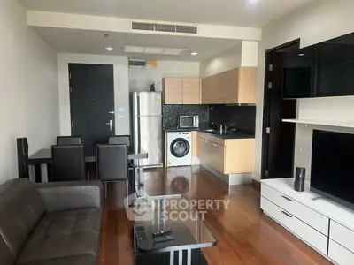 Modern open-layout living room with sleek kitchen and dining area, featuring hardwood floors and contemporary furnishings.