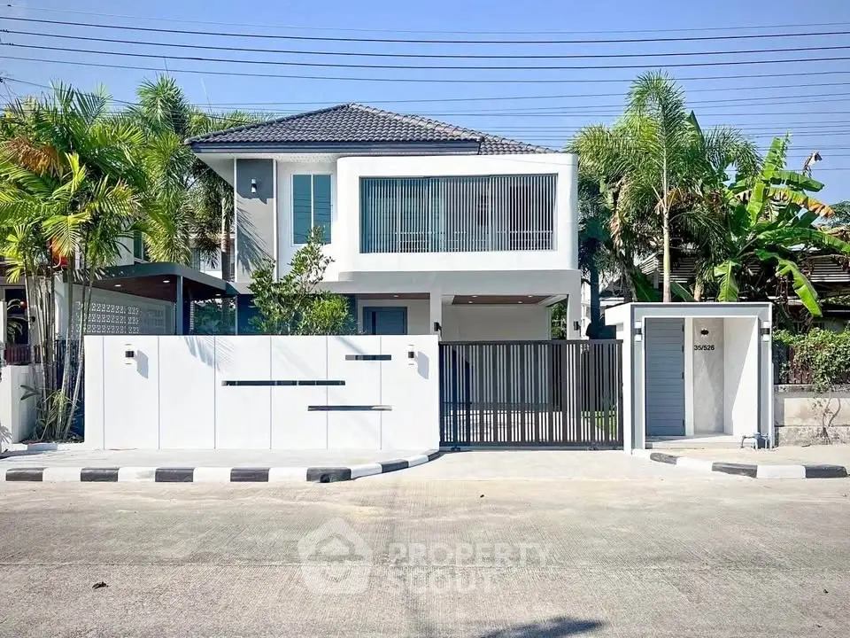 Modern two-story house with sleek design and gated entrance, surrounded by lush greenery.