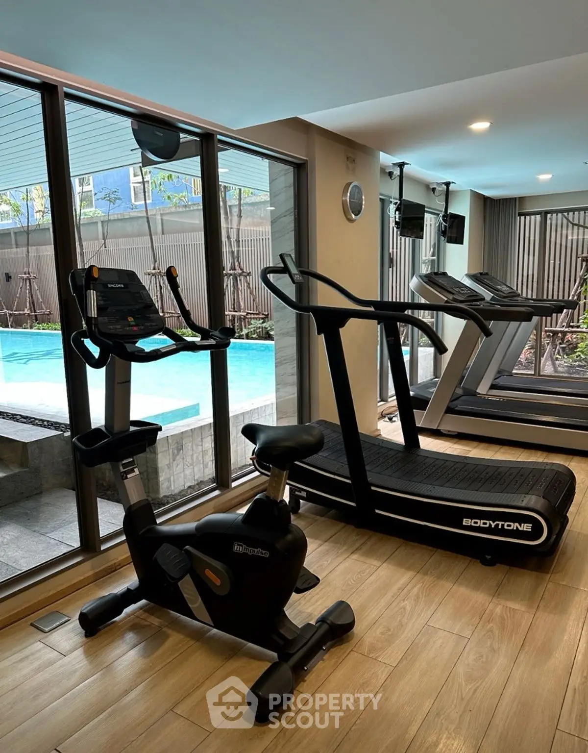 Modern gym with pool view featuring exercise bike and treadmills in luxury condo.