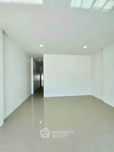 Spacious empty room with glossy tiled floor and recessed lighting, perfect for customization.