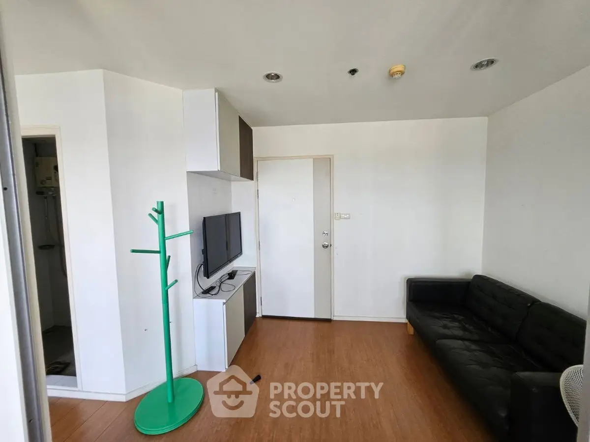 Modern living room with sleek black sofa and wall-mounted TV, featuring minimalist design and wooden flooring.