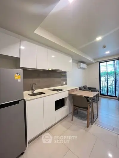 Modern kitchen with sleek white cabinets and dining area in open layout apartment.