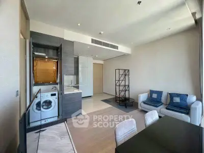 Modern living room with open kitchen and washing machine, featuring stylish furniture and ample natural light.