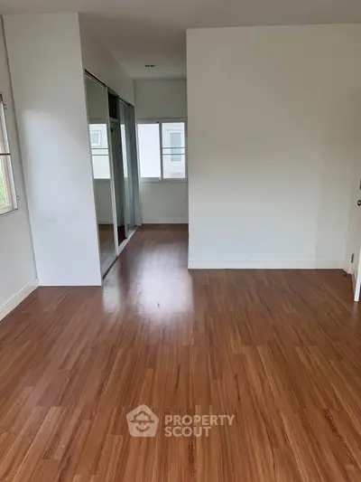 Spacious empty room with wooden flooring and mirrored closet doors