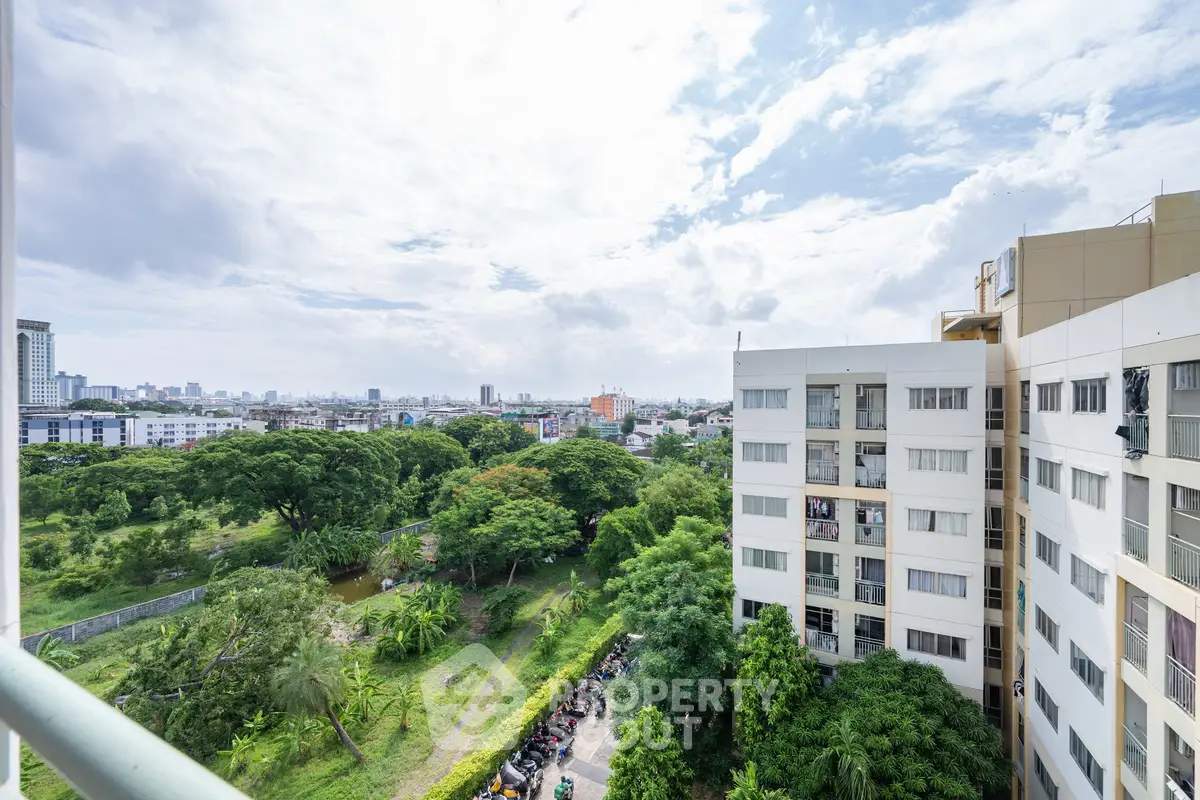 Stunning cityscape view from a high-rise apartment balcony overlooking lush greenery and urban skyline.