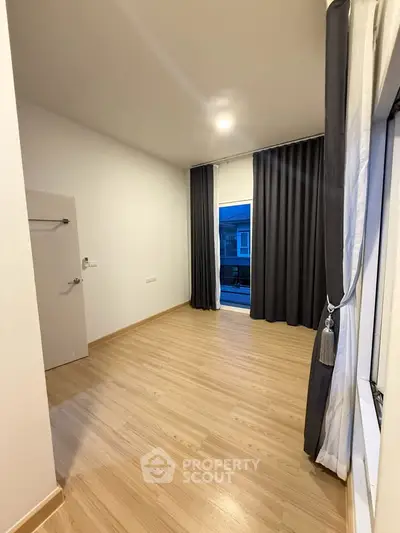 Spacious empty room with wooden flooring and large window, ideal for customization.