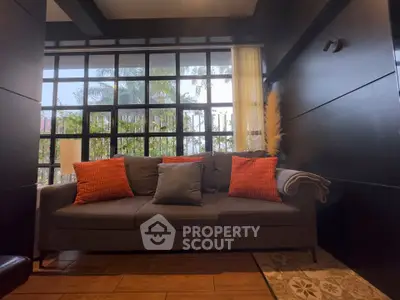 Chic living room with modern sofa and large windows offering lush garden views.