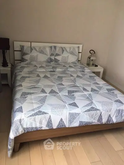 Cozy bedroom with modern geometric bedding and wooden flooring, perfect for relaxation.