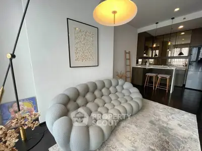 Modern living room with unique sofa and open kitchen layout, featuring stylish decor and contemporary lighting.