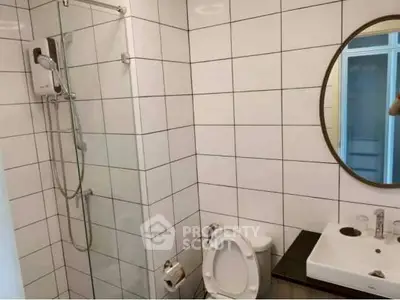 Modern bathroom with white tiles and round mirror, featuring shower and sink.