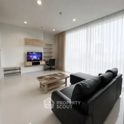 Spacious modern living room with sleek black sofa and entertainment center, featuring large windows and ample natural light.