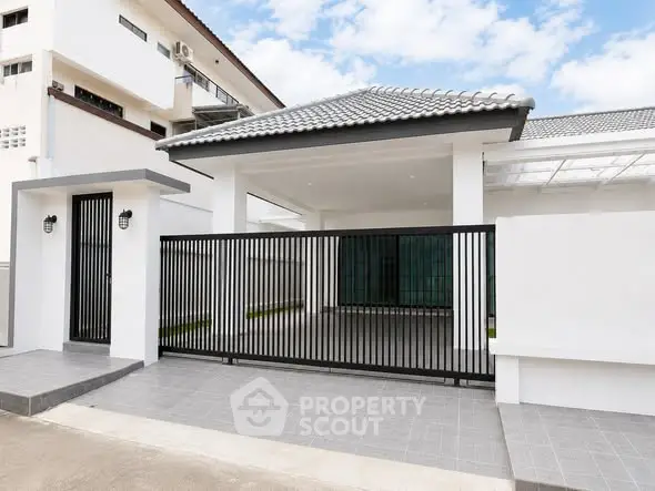 Modern white house exterior with sleek black gate and tiled driveway under a clear blue sky.