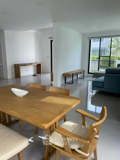 Spacious modern living room with wooden dining set and large windows offering natural light.