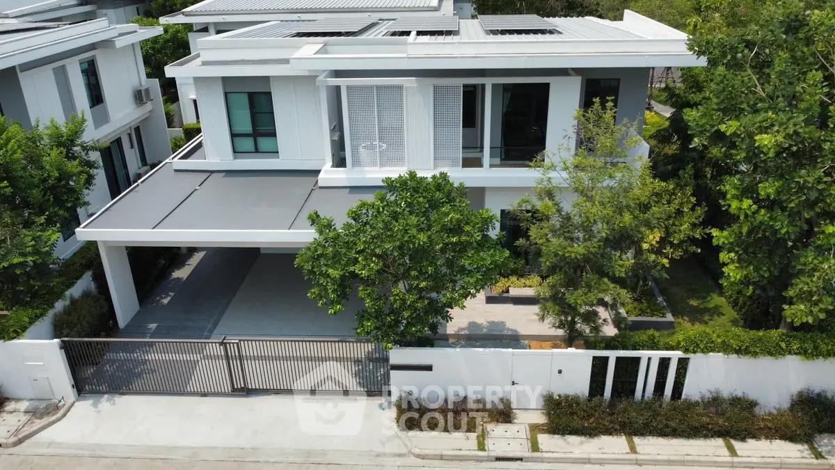 Modern two-story house with sleek design and spacious driveway in lush green setting.