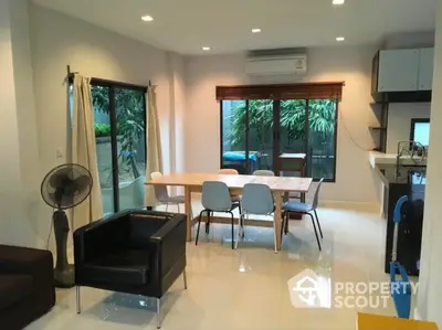 Modern dining area with sleek furniture and large windows overlooking lush greenery.