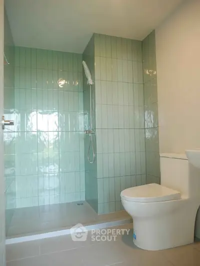 Modern bathroom with sleek shower and toilet in stylish green and white tiles.