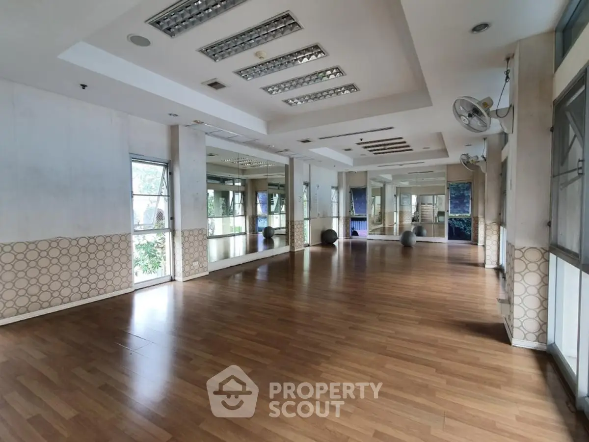 Spacious gym with wooden flooring and mirrored walls in modern building.
