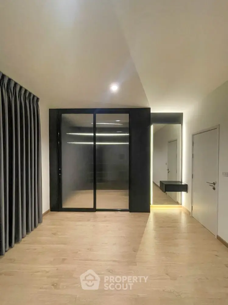 Spacious and modern living area with sleek black sliding doors leading to a well-lit room, featuring warm wooden flooring and minimalist design.