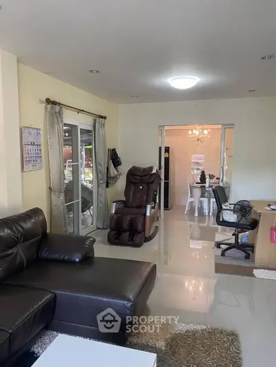 Spacious living room with leather sofa and massage chair, leading to dining area.