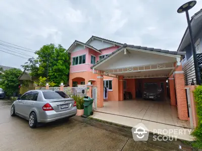 Charming two-story pink house with spacious carport and lush greenery in a serene neighborhood.