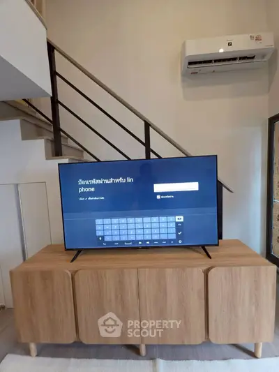 Modern living room with stylish wooden cabinet and sleek TV under a staircase, featuring a wall-mounted air conditioner.