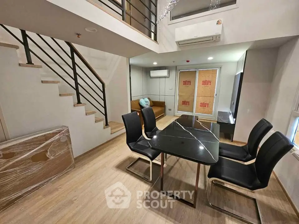 Modern duplex interior with stylish dining area and staircase, featuring sleek black chairs and elegant table.