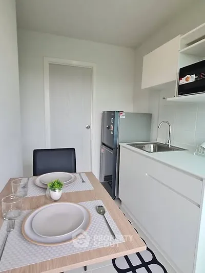 Modern compact kitchen with dining area, featuring sleek white cabinetry and a small fridge.