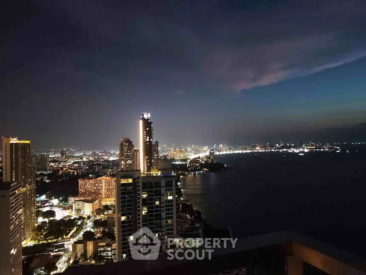 Stunning cityscape view from a high-rise balcony overlooking the ocean at night.