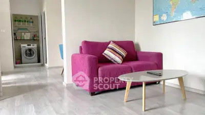 Modern living room with vibrant pink sofa and sleek coffee table, adjacent to a laundry area with washing machine.