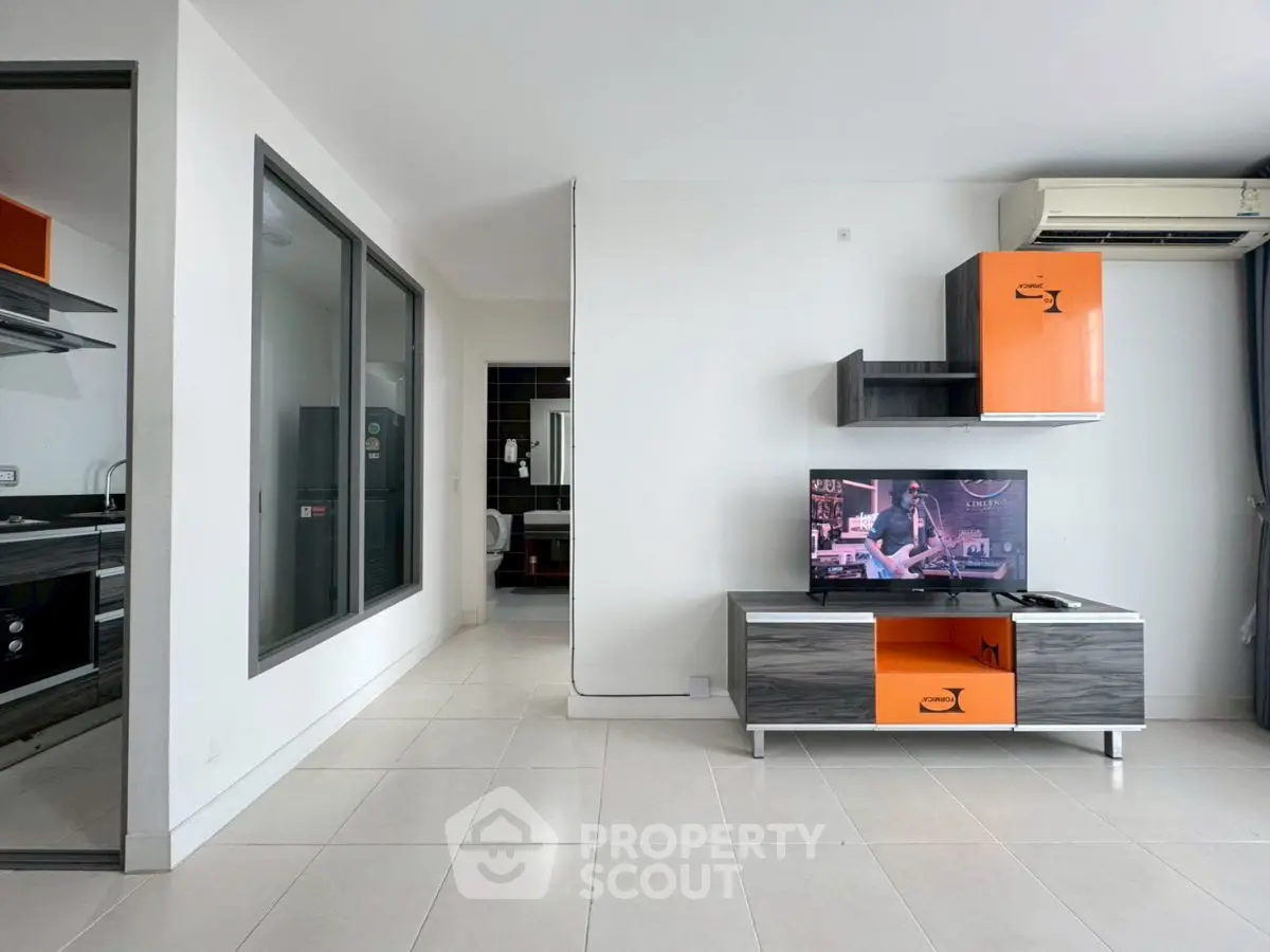 Modern living room with sleek TV unit and air conditioning, adjacent to a stylish kitchen.