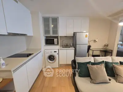 Modern apartment interior with compact kitchen and cozy living area, featuring washing machine and sleek appliances.