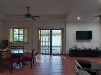 Spacious living room with red tiled flooring, large windows, and a ceiling fan, leading to a sunny balcony with a view.