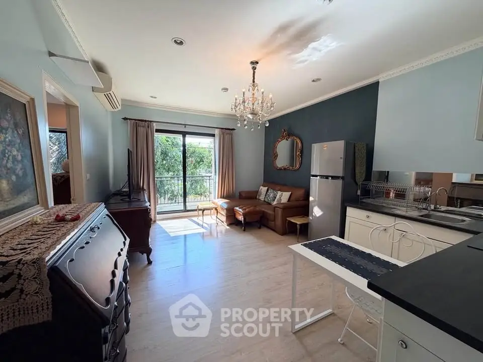 Charming living room with elegant decor and open kitchen layout, featuring a chandelier and natural light.
